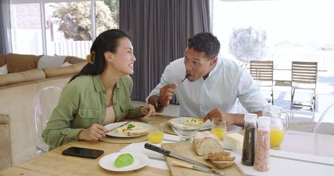 Couple sharing sunny breakfast at modern dining table, eating eggs with avocado and juice