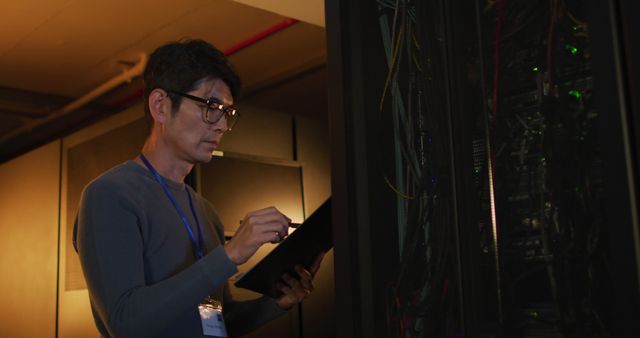 IT technician checking server rack with a clipboard in hand. Ideal for depicting the roles of IT professionals in maintaining and managing extensive technology infrastructure. Useful for articles, blogs, or websites discussing data centers, IT job roles, or network maintenance processes.