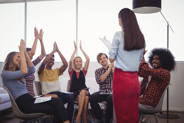 Businesswoman standing in front of her team, who are cheering and applauding her in an office setting. This image can be used to depict themes of teamwork, success, motivation, and corporate culture. Ideal for business presentations, corporate websites, and motivational materials.