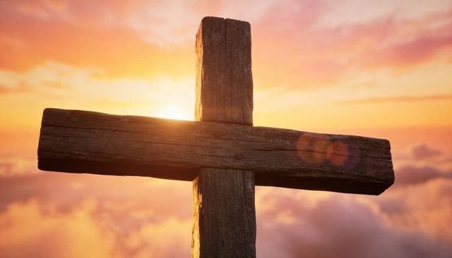 Standing weathered wooden cross backlighting sunrise over clouds with warm lens flare