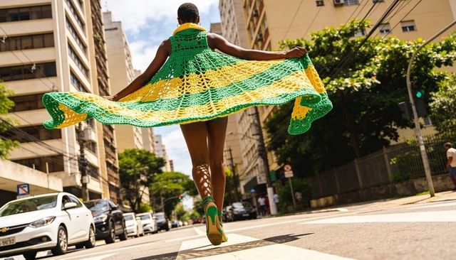 Leaping woman wearing green and yellow crocheted cape over urban crosswalk showing motion