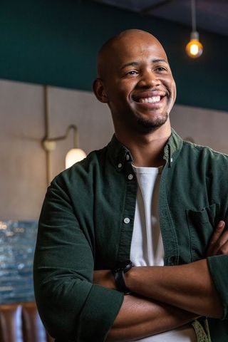 Confident african american man smiling with arms crossed in casual cafe interior