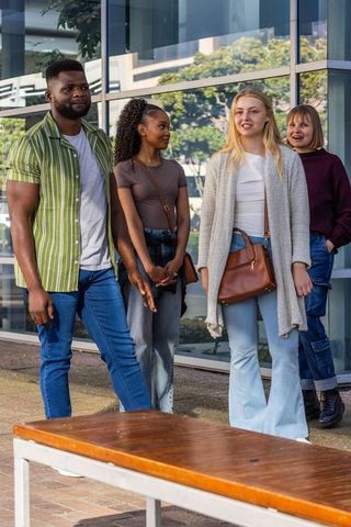 Diverse friends walking and chatting by modern glass building, casual urban lifestyle