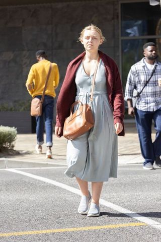 Urban woman walking crosswalk in blue dress maroon cardigan carrying brown leather satchel