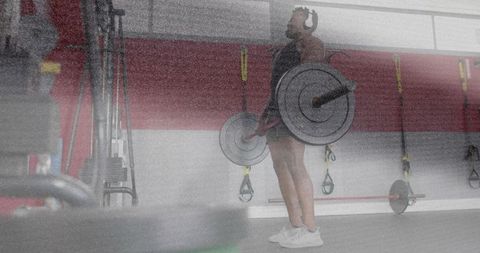 Mid-adult man performing barbell deadlift with headphones in gym for strength training