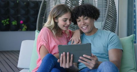 Young Couple Sharing Tablet on Couch Laughing Together