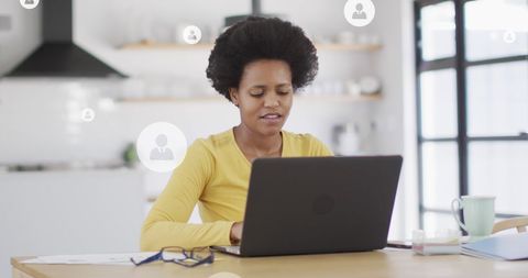 African American Woman Using Laptop in Modern Kitchen with Digital Icons