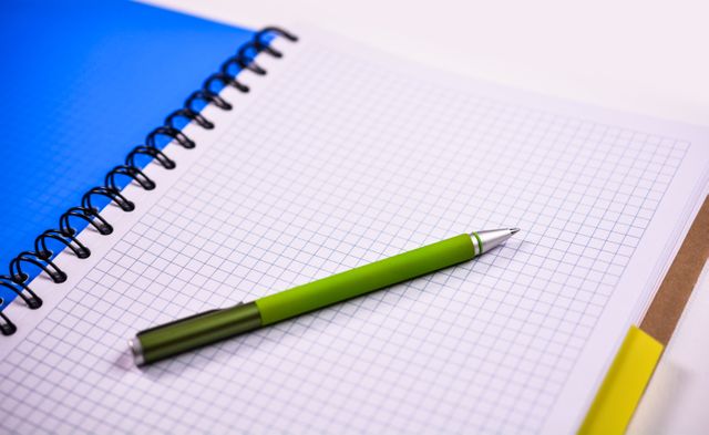Green pen lying on open grid notebook with blue cover. Ideal for back-to-school promotions, office supplies, educational content, and stationary-related marketing.