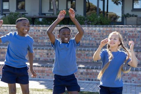 Joyful diverse elementary students playing outdoors in matching blue shirts on school lawn