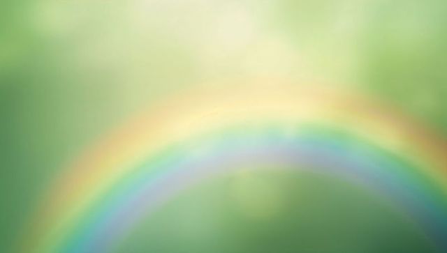 Curving prism rainbow over soft green bokeh backdrop with warm sun flare and haze