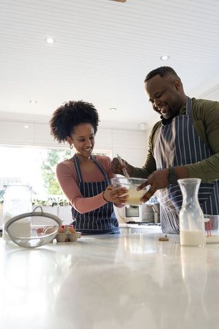 African american couple whisking batter on marble countertop wearing striped aprons