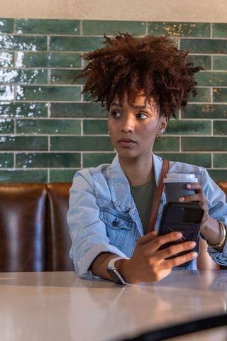 African american woman using smartphone and coffee in cozy cafe with green tile wall