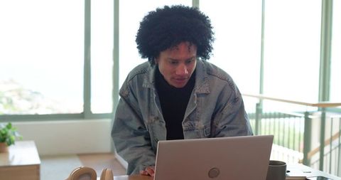 Man in Denim Jacket Working Remotely on Laptop in Bright Modern Home Office