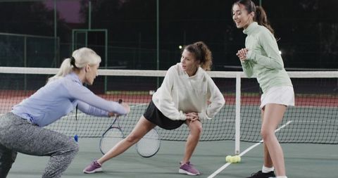 Women warming up on tennis court at twilight practicing dynamic team drills