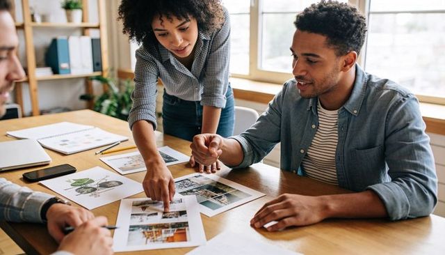 Creative team reviewing print mockups and layouts around wooden table in bright office