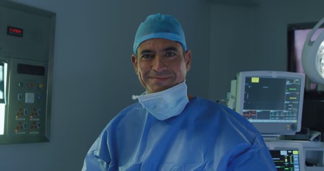 A confident surgeon wearing blue scrubs, a face mask, and cap, standing in an operating room surrounded by medical equipment. Ideal for use in medical and healthcare-related websites, advertisements, hospitals' promotional materials, educational podcasts about surgery, and health articles.