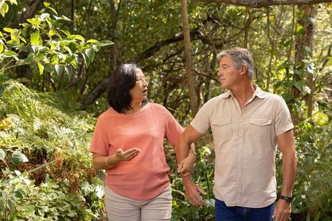 Senior couple holding arms walking wooded trail enjoying peaceful nature stroll