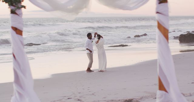 Couple all dressed in white having their first dance on a beautiful beach looks perfect for wedding and romance themed media. Ideal for blogs, wedding planning websites, and love-inspired advertisements. Shows serenity, joy of sunset, ambient peaceful scene for relaxation, positivity campaigns.