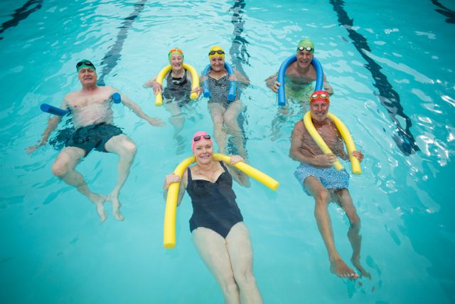 Senior adults are enjoying a water aerobics class using pool noodles in a swimming pool. They are smiling and appear to be having fun while engaging in a healthy and active lifestyle. This image can be used for promoting senior fitness programs, aquatic exercise classes, and healthy living for the elderly.