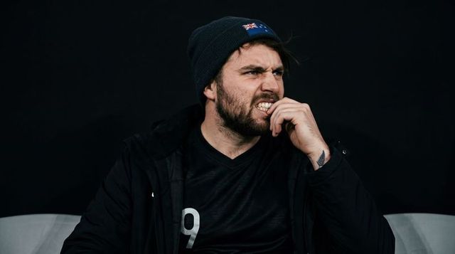 Tense bearded athlete biting nails on bench wearing beanie, jacket and number 9 jersey