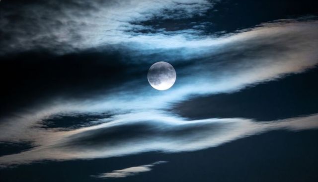 Full Moon Casting Blue Glow Through Layered Clouds Over Dark Night Sky