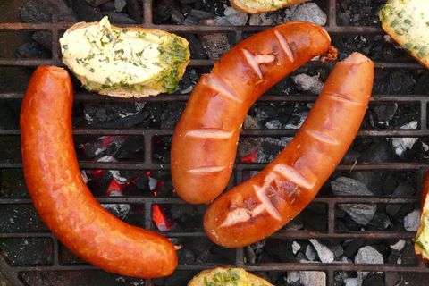 Grilling smoked sausages on charcoal grill with herb garlic bread