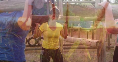 Women demonstrating team spirit by tackling obstacle course with wooden logs