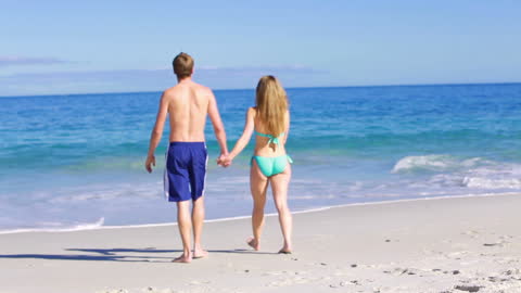Couple Strolling Hand in Hand on Sunny Beach Waterside