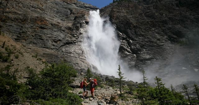 Hikers Admiring Majestic Waterfall in Mountainous Terrain on Sunny Day - Download Free Stock Images Pikwizard.com