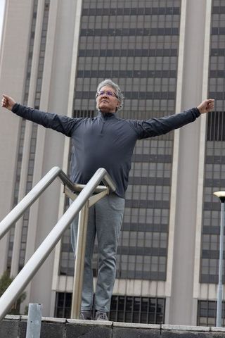Senior man standing arms outstretched on urban steps between handrails by office tower