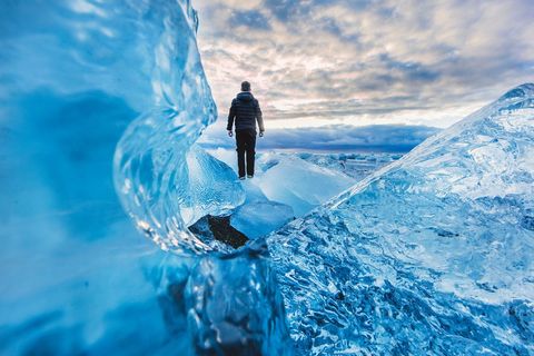 Traveler Standing on Crystal Icebergs under Dramatic Arctic Sky at Sunset