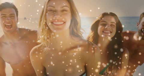 Sunlit friends smiling and laughing on beach shoreline, posing in swimwear with ocean bokeh