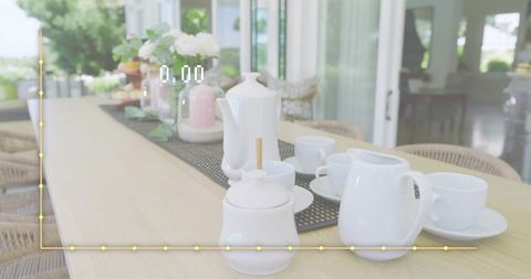 Displaying white ceramic tea set on sunlit veranda table with garden view and yellow graph
