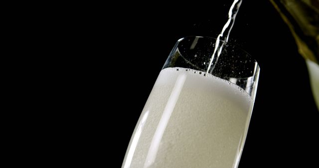 Pouring sparkling champagne into a flute glass, creating bubbles and a foamy top against a black background. Ideal for use in advertisements, party invitations, festive occasions, or articles about celebrations and luxury beverages.
