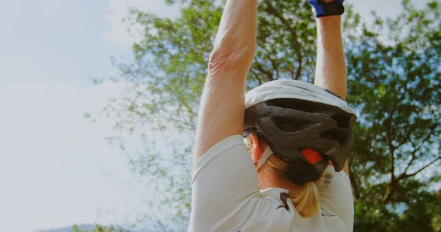 Cyclist raising arms in victory wearing helmet and sports attire celebrating outdoors. Ideal for promoting cycling gear, outdoor sports activities, and motivational content related to fitness and achievement.
