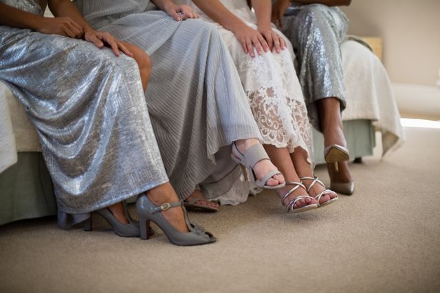 Bride and bridesmaids sitting together on a sofa, showcasing their elegant dresses and high heels. Perfect for use in wedding planning materials, bridal magazines, fashion blogs, and advertisements for wedding attire or accessories.