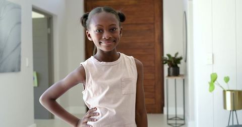 Confident african girl posing and smiling with hand on hip in modern minimalist entryway