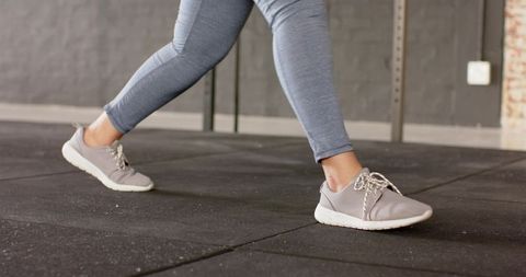 Forward lunge in gray leggings and sneakers on black gym floor for strength and mobility