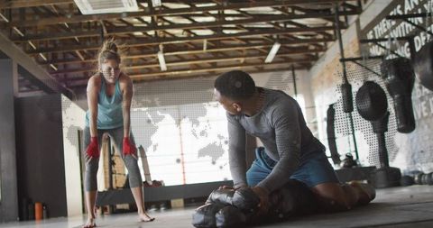 Woman training boxing with coach holding pad, red hand wraps, industrial warehouse gym