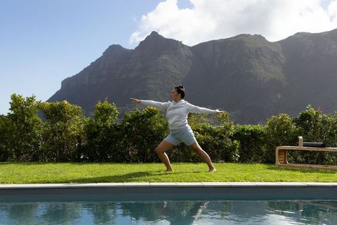 Mid-30s asian woman practicing yoga poolside backyard with mountain view and greenery