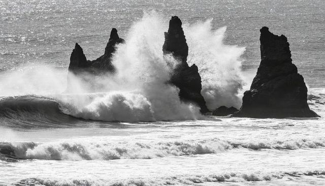 Black and white waves crashing against jagged sea stacks sending towering spray and foam