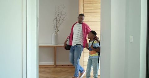 African american father walking son into home foyer carrying shoulder bag and backpack