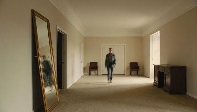 Walking man in minimalist living room with gold floor mirror and wooden desk in daylight