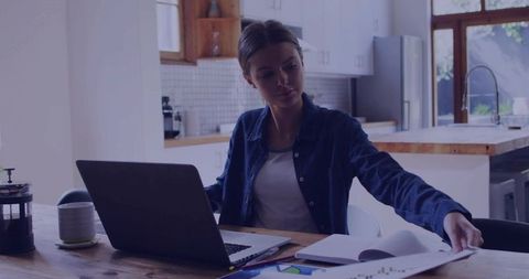 Focused woman reviewing report on laptop in modern kitchen