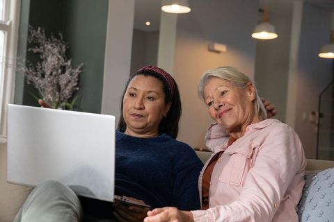Senior women using laptop and smartphone on cozy sofa sharing warm companionship at home