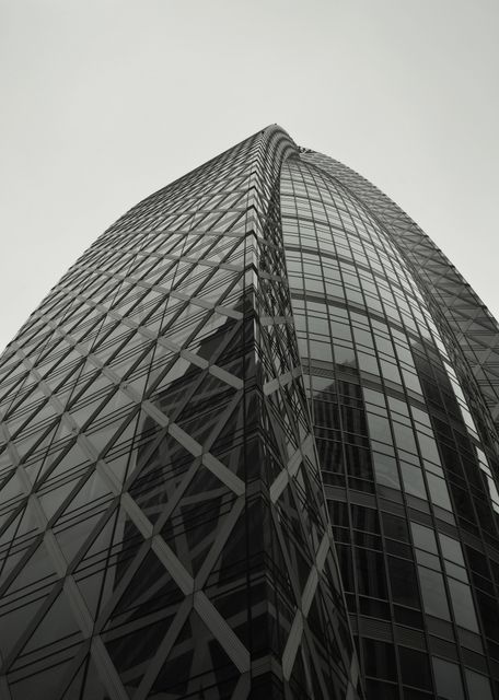 This image captures a modern skyscraper with a sleek glass facade and unique architectural design. Ideal for use in real estate advertisements, architectural showcases, corporate presentations, or urban development materials.