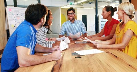 Man leading creative team brainstorming session at modern glass-walled conference table