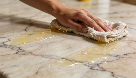 Hand wiping sticky spill from marble countertop with rag closeup cleaning kitchen surface