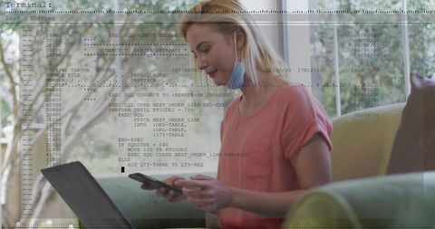 Working from home holding phone and tapping laptop on sofa with mask and code overlay