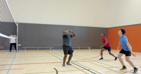 Indoor volleyball team training players tracking ball near net in gym